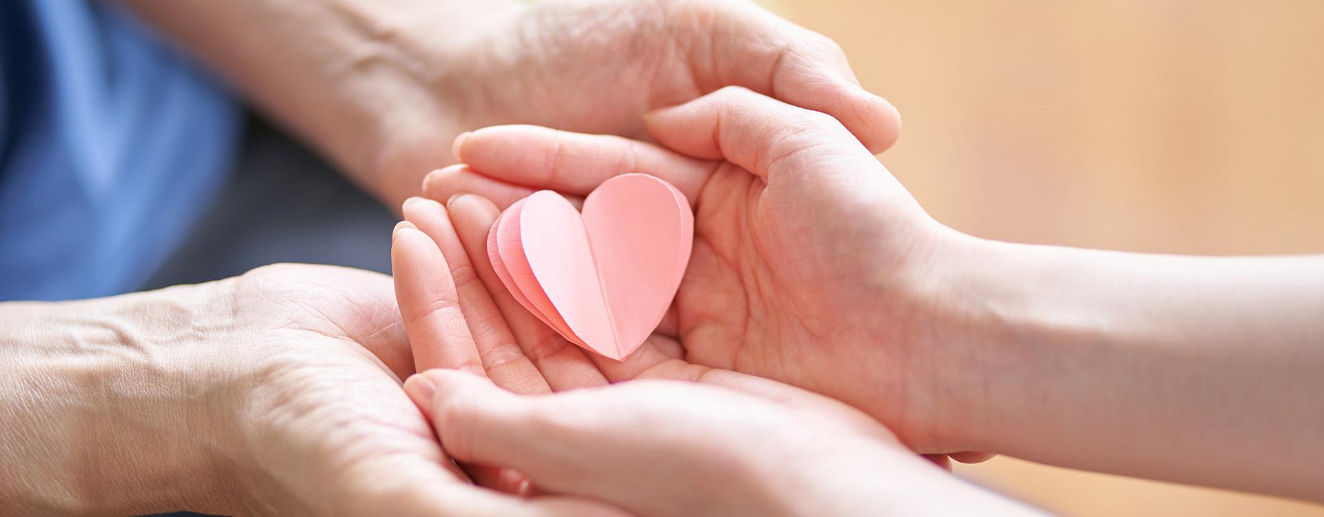 Young woman holding paper heart in hands of another person